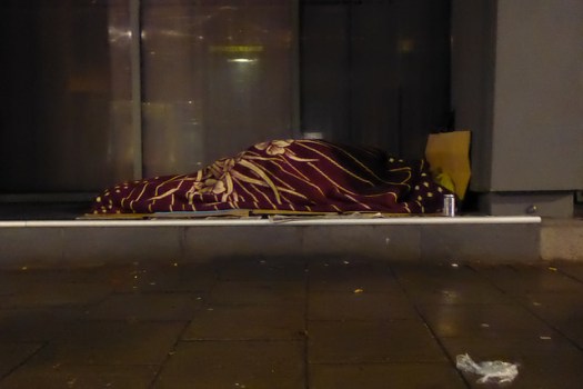 Someone sleeping on the street under a blanket.